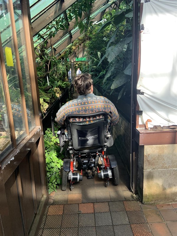 Image of a person in a power chair going down a corridor inside the greenhouse.