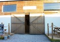 Entrance to the barn. Gravel surface to large wooden doors. They do open quite wide but then there are more doors inside and a small step up.