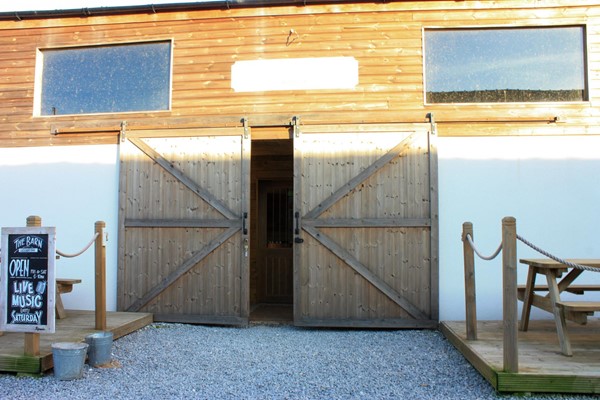 Entrance to the barn. Gravel surface to large wooden doors. They do open quite wide but then there are more doors inside and a small step up.