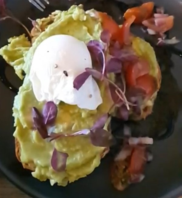 Smashed Avacado on sourdough bread with red onion, tomato, garlic, drizzled with balsamic glaze and decorated with edible flowers