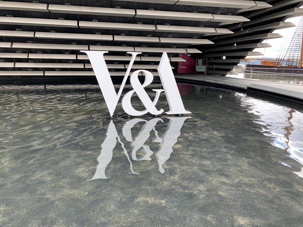 The white V and A sign sitting in the middle of one of the ponds outside the buildings main entrance