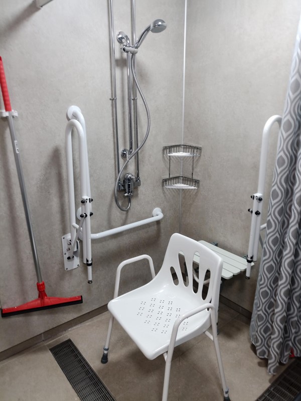 Accessible shower with fold down seat plus plastic moveable seat. There is a curtain around the shower area.