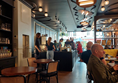 the view from the back of the cafe, looking towards the counter and the front window. There is a clear path between tables. the floor is wood and smooth, with no obstacles.