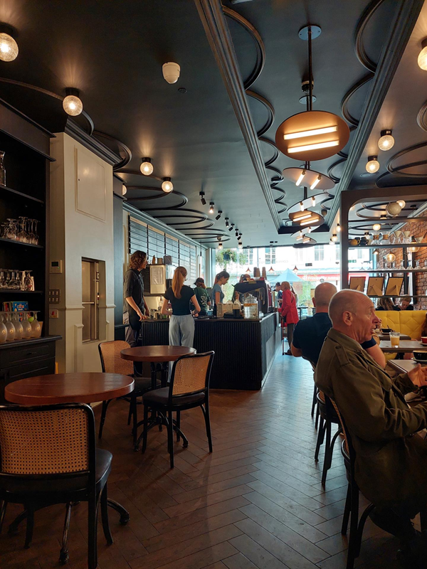 the view from the back of the cafe, looking towards the counter and the front window. There is a clear path between tables. the floor is wood and smooth, with no obstacles.
