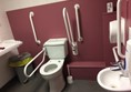 Accessible toilet with plenty of grab rails and red cord hanging freely to the floor. There is also plenty of room to move around plus have carers in.