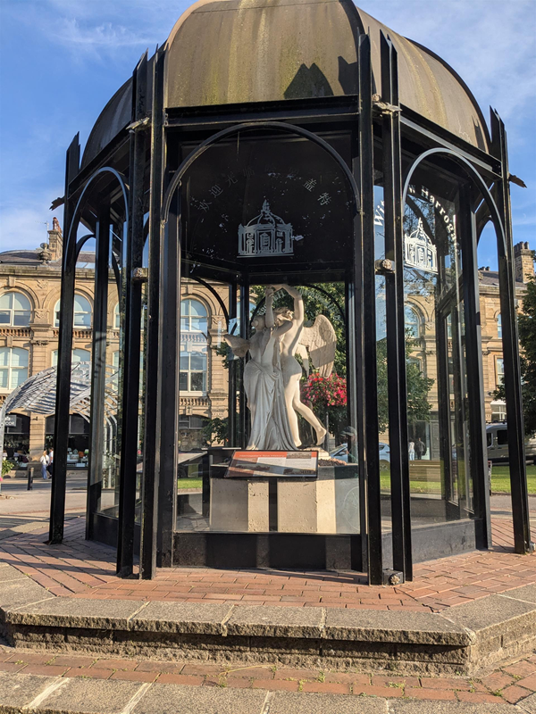 Image of a pavilion, inside which is a marble statue of two winged figures embracing.
