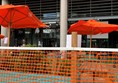 View from outside beer garden. There is orange netting around the plants to stop people walking in between. In the distance a member of staff is wearing a mask.