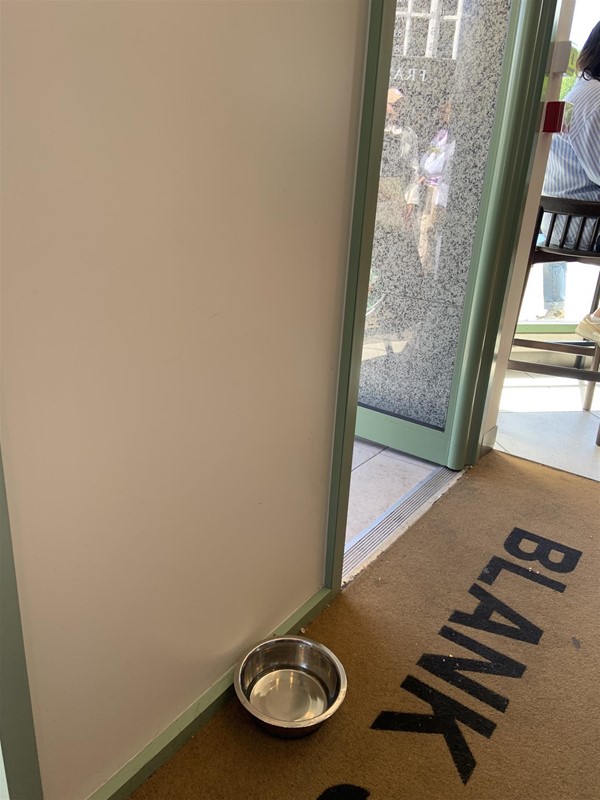 Image of  a metal dog bowl on the floor in between the two doors just inside the entrance.