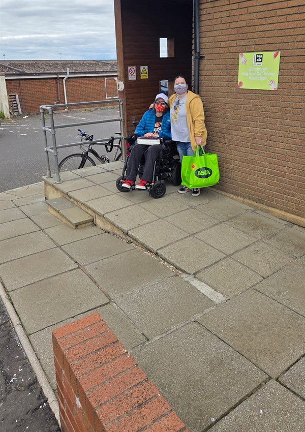 Two people at the top of an access ramp, one person in a powerchair.