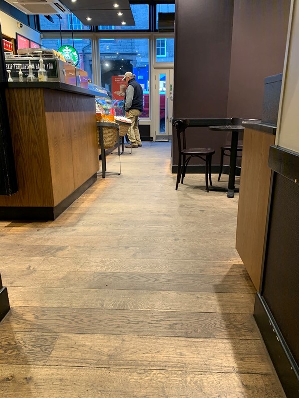 Image of the shop floor from the perspective of coming out of the toilet. There is space between the counter and tables of the shop but a narrow part where a wall sticks out.