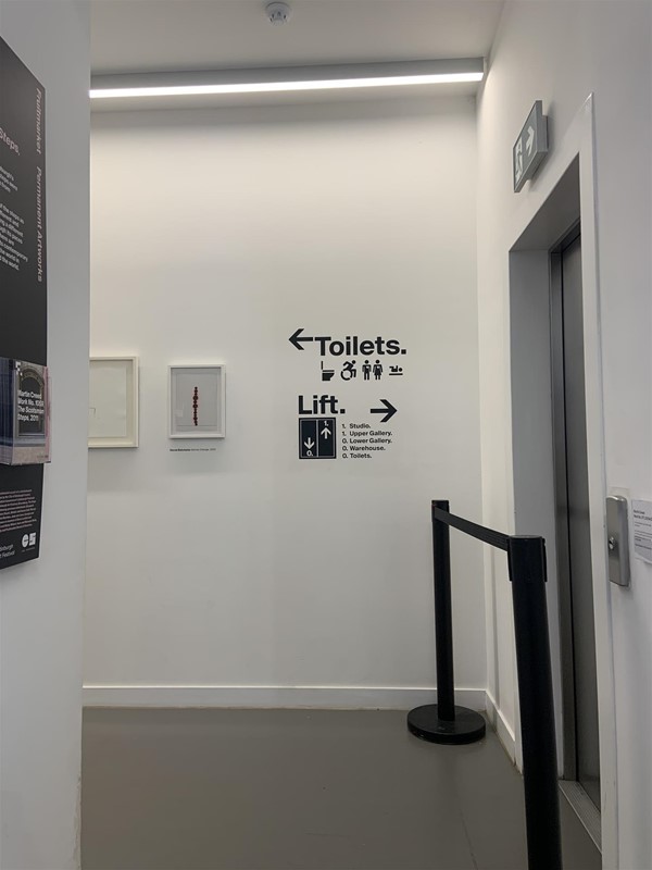 image of a corridor turning to the left with a sign pointing to the toilets on the left and the lift on the right
