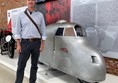 Image of a man standing next to a silver vehicle on display.