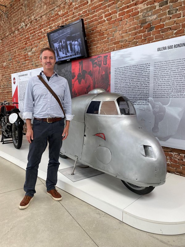 Image of a man standing next to a silver vehicle on display.