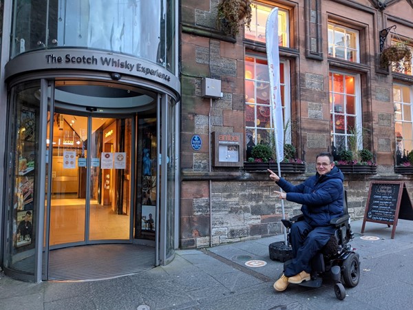 Paul sitting outside the Scotch Whisky Experience pointing to the door and smiling broadly.
