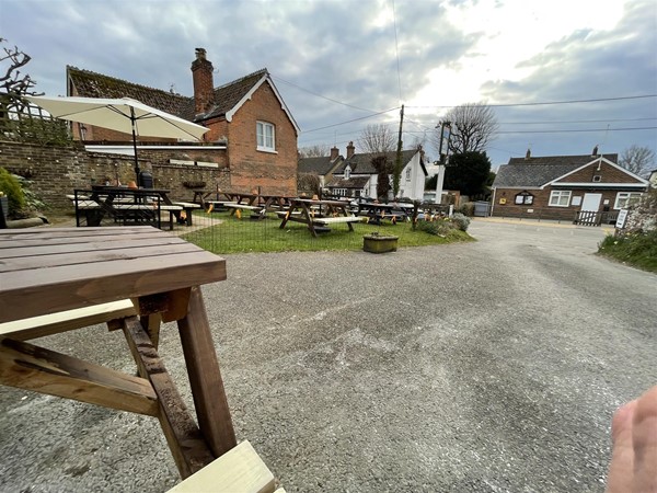 Front of the pub with outside seating and village hall opposite with accessible wc