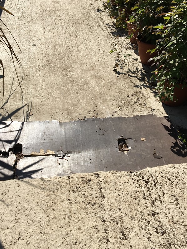 Pieces of hardboard (or similar inappropriate material) laid to try to cover a large gap between two concrete walkways. Where the material is unsuitable and has gotten wet it has buckled and fallen into the gap so offering no support to cross it.