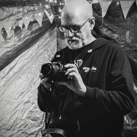Me , male, grey goatee, shaven head, glasses.  Examining a DSLR.