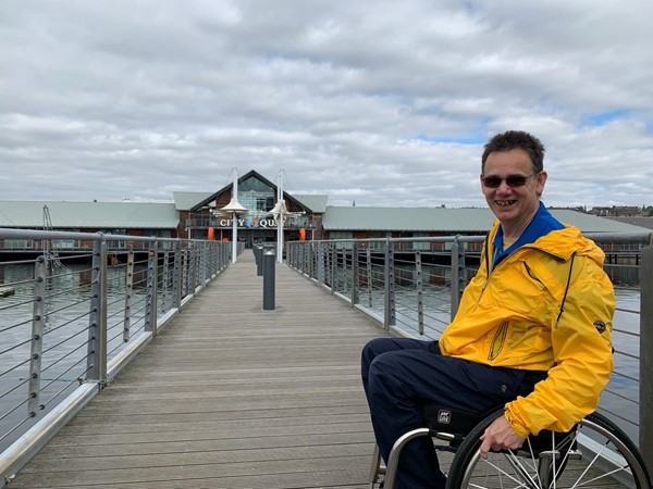 Paul wheeling across the walkway over the water of the harbour basin.