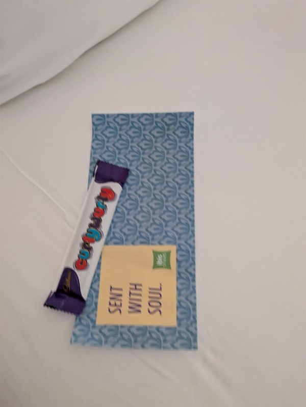 Image of a Curly Wurly Chocolate bar on the bed sheet on top of a slip of paper reading Sent with Soul