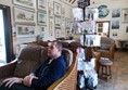 Man sitting on sofa with a stand behind him selling crafting items.