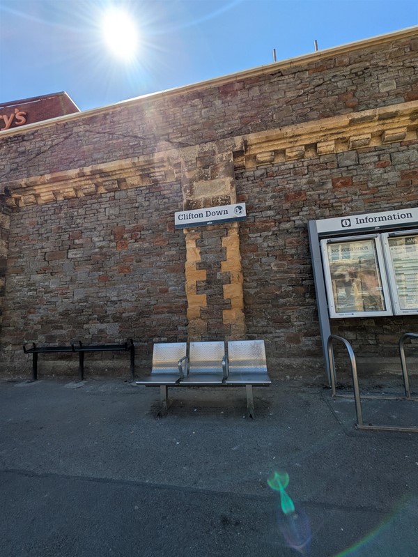 Image of metal seats on platform below a sign marked Clifton Down