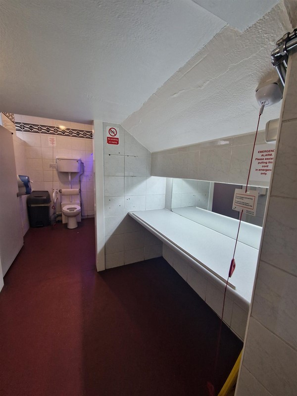 An even wider view of the accessible toilet showing the layout, including the toilet, grab rails, sink, and available space.
