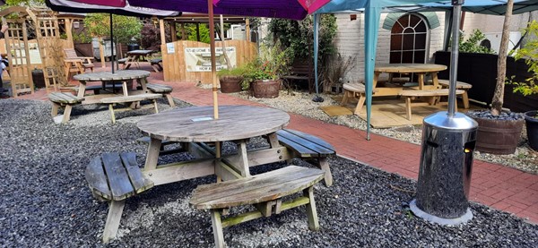 Picture of outdoor seating. A wooden round table with benches and an umbrella