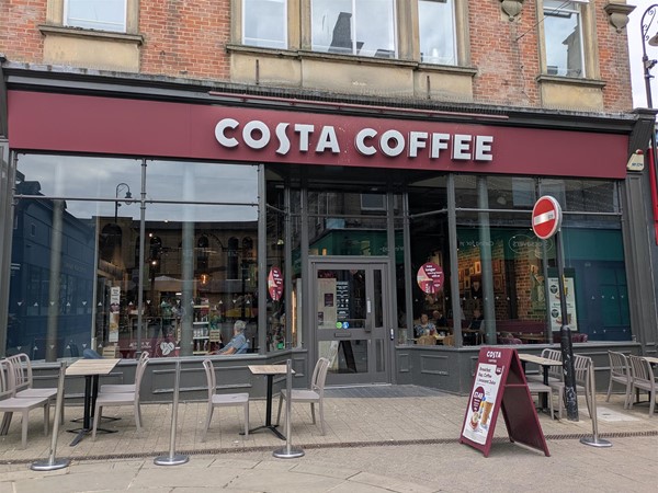 Image of exterior of Costa Coffee, white letters on a red background show the name of the location.