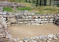 Ruins of a Roman room with fencing and steps in the background.