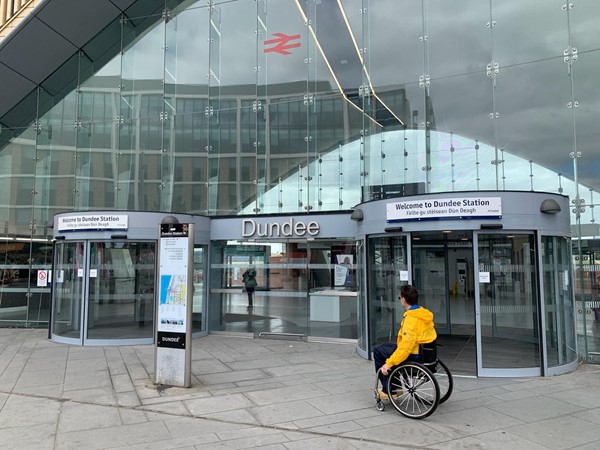 Paul wheels toward the automatic doors at the main entrance of Dundee railway station