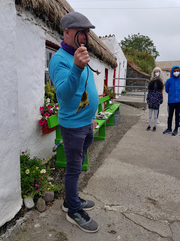 Famine Village guide giving demonstrations of local food and customs outside the traditional house where he lived as a child. You can see the ramp up to the accessible toilet at the back of the picture