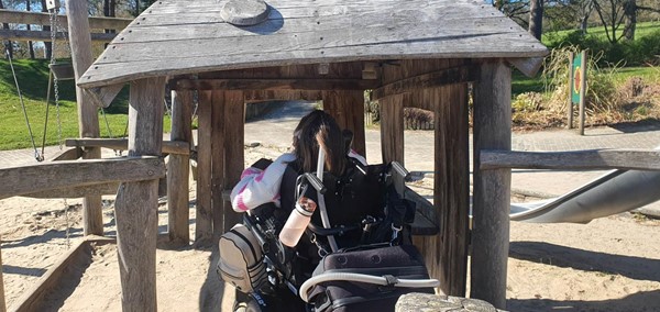 Picture of Claire in her wheelchair in the wooden hut play area