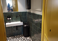 A view of the accessible toilet, looking through the open door, the easy-to-use sink is visible, as is the beautiful geometric-tiled floor. The mirror is standing height and the hand towlels are within reach but above the sink.