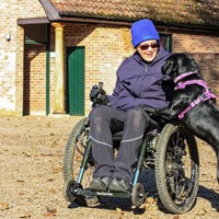 Lady in mountain trike with dog jumping up on her lap at the side. She is in winter coat and hat ready to go hiking.