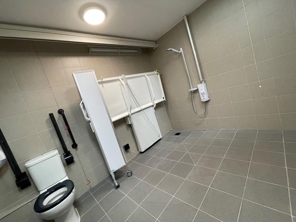 Inside the Changing Places toilet, showing the adult sized changing bench and the adjacent shower unit