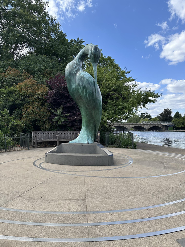 Image of a heron statue located nearby and next to the water with some wooden benches