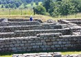 Ruins in the foreground with grass bank showing that the fence is raised above the ruins.