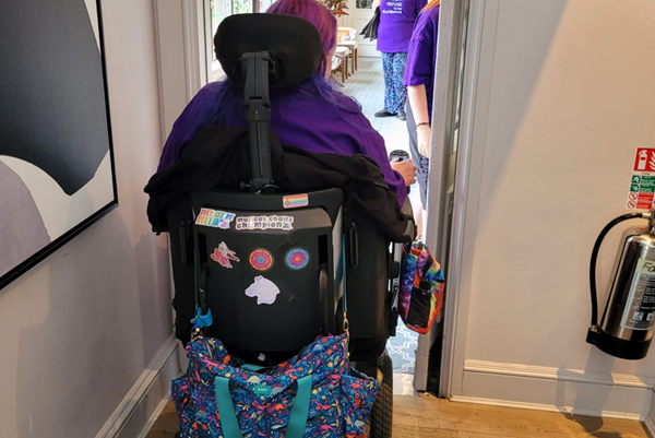 Wheelchair user unable to get through a door to access meeting rooms and toilets. (Bag was removed  from the side arm and the chair still didn’t fit through).