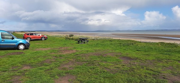 Picture of a grassy shoreline with two parked cars and a wooden picnic bench