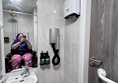A wheelchair user taking a photo is shown in the mirror. In front is a sink and hairdryer. To the right there are hand towels that can only be accessed by a tall standing person.