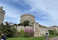 outdoor view of the large bailey tower in the centre of Windsor castle, built from stone constructed on a tall hill. The sky is blue with wispy clouds and there are colourful well-tended plants in bloom, a lovely spring day, some other tourists are walking through the shot. The path is smooth.