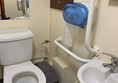 View of accessible toilet from door showing red cord , handrails and sink