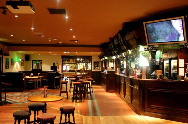 Picture of Old Bar - you can see a bar to the right, a number of tables and chairs, a booth in the corner, and a TV screen above the bar