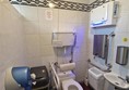 Inside the accessible toilet. A sanitary bin is positioned right next to the toilet, which could make wheelchair transfers difficult. A small sink and paper towel dispenser are visible on the right, with a wall-mounted grab rail.