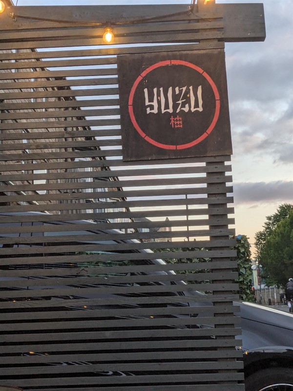 Image of Yuzu signage on a partition outside the venue. The letter are stylised, white text on with a read circle.