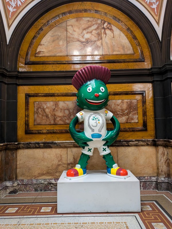 Image of "Clyde" statute, a green mascot with purple hair resembling a thistle