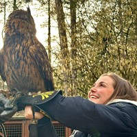 Molly has a large owl perched on her arm and smiles up at it