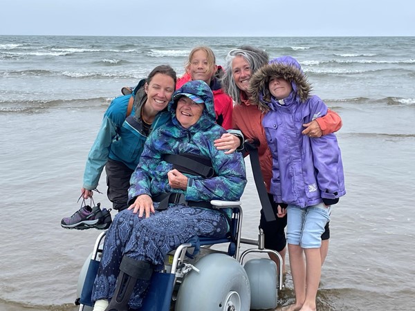 A group of people standing behind a person in a wheelchair on a beach