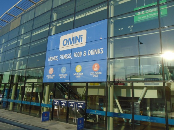 The exterior of the Omni Centre, with a sign saying Omni, Movies, Fitness, Food, and Drinks.