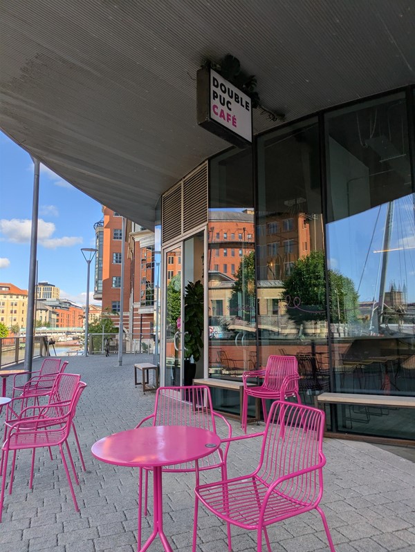 Image of pink metal seats and pink tables outside of the café